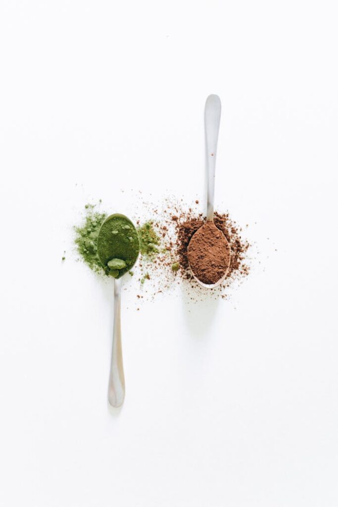 Top view of two teaspoons with green matcha and brown cocoa on white background.