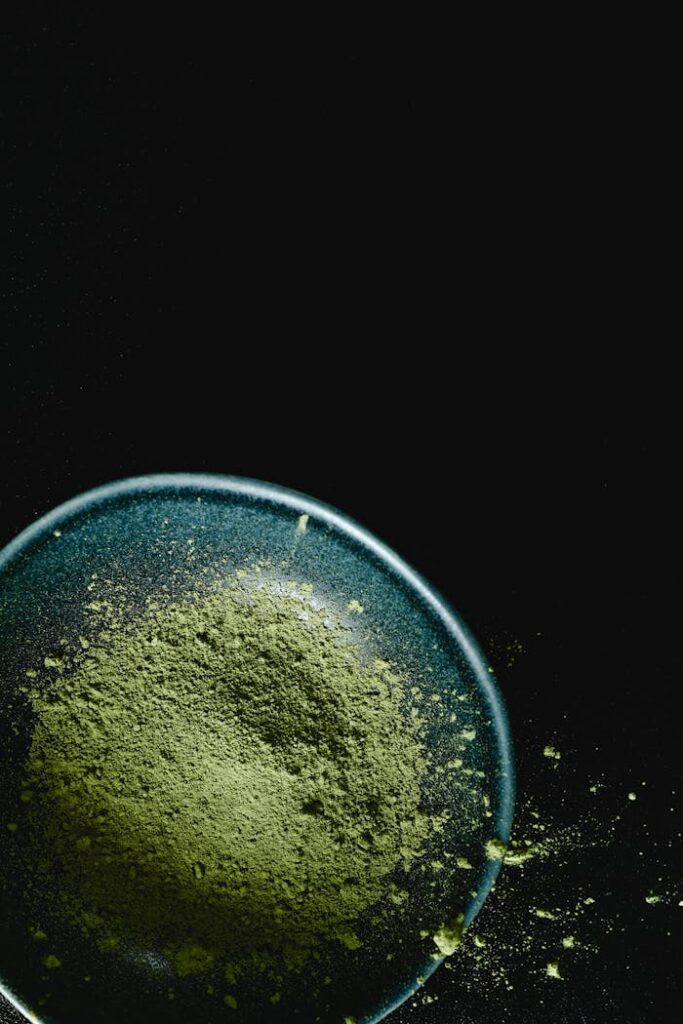 High-quality organic matcha powder displayed in a blue ceramic bowl against a dark background, showcasing its texture and vibrant color.